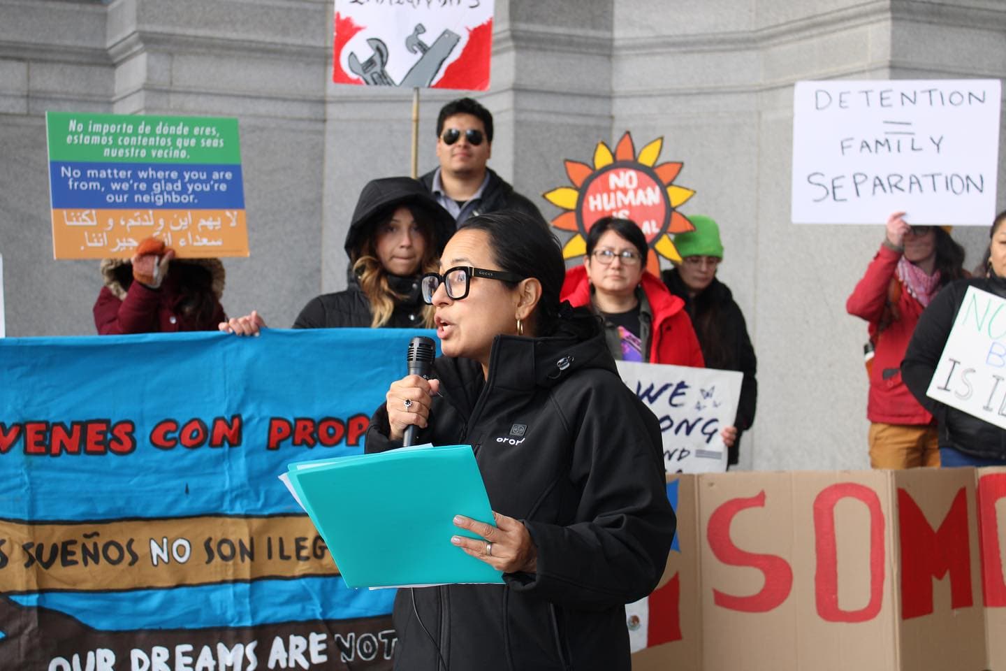 Photo: Casa San Jose - Rally speaker with crowd, banners, and signs behind