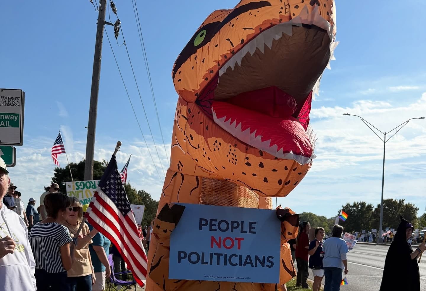 Inflatable dinosaur holding a People Not Politicians sign